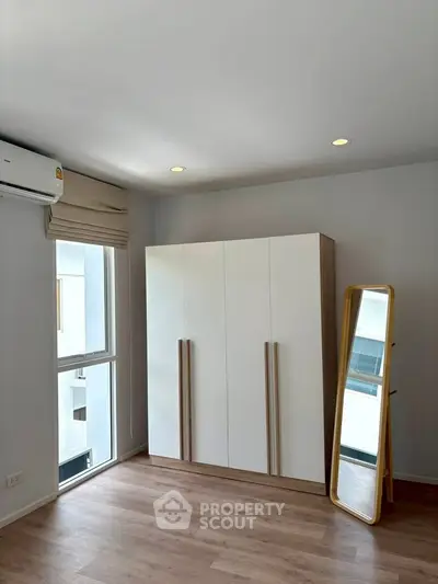 Modern bedroom with sleek wardrobe and full-length mirror, featuring natural light and wooden flooring.