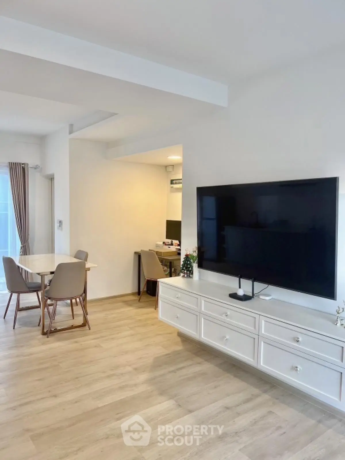 Modern living room with large TV and dining area, featuring stylish furniture and wooden flooring.