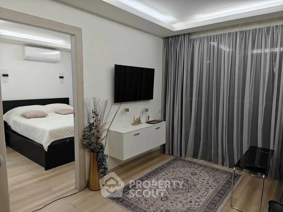 Modern living room with TV and view into cozy bedroom, featuring elegant decor and stylish furnishings.
