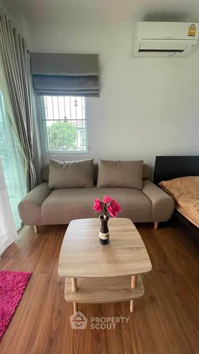Cozy living room with modern sofa and wooden coffee table, featuring air conditioning and natural light.