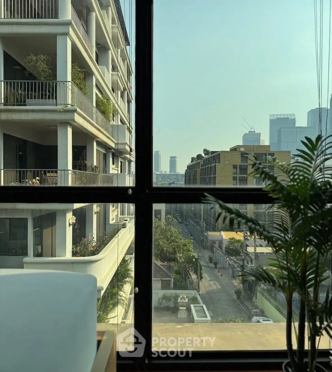 Stunning urban view from modern apartment window with lush balcony greenery.