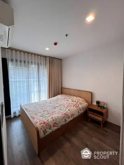 Serene bedroom with ample natural light, featuring a large bed with floral bedding, modern lighting, and elegant floor-to-ceiling curtains.