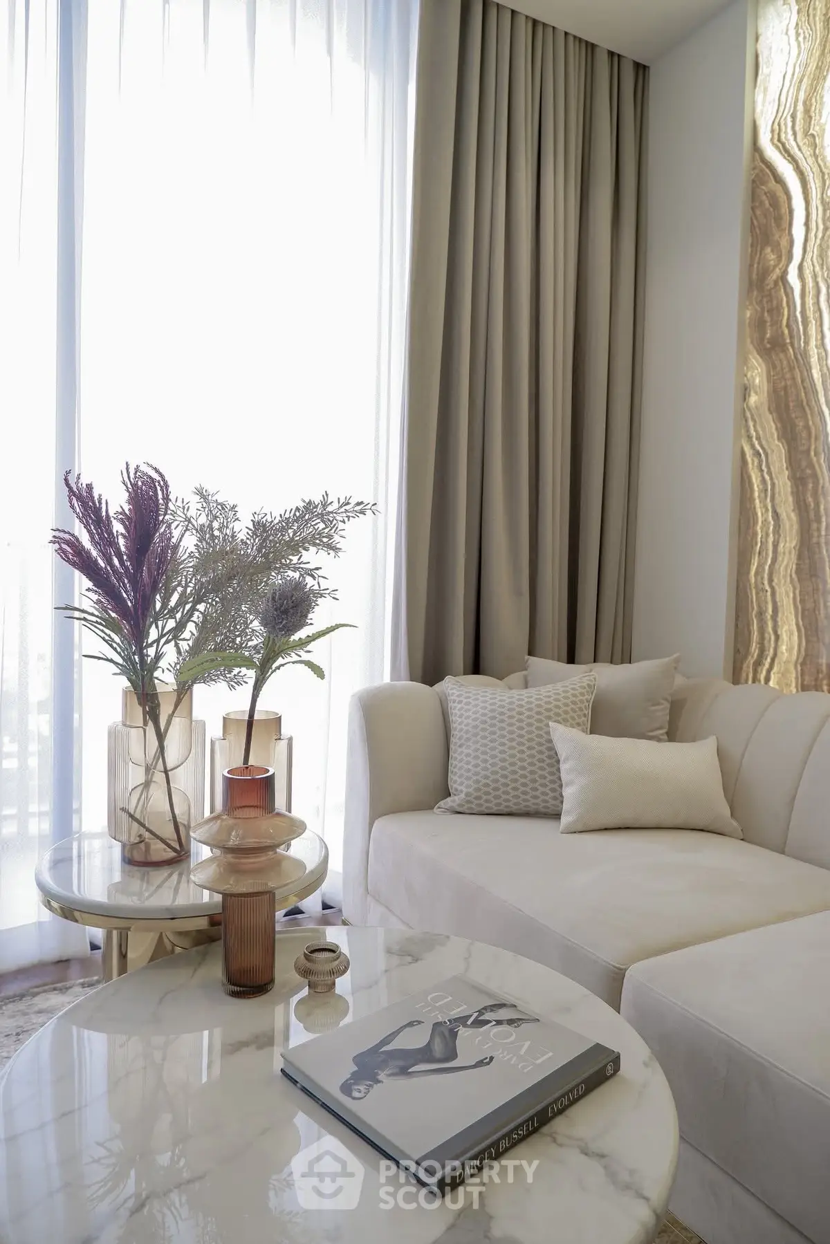 Elegant living room with plush sofa and stylish decor, featuring a marble coffee table and floor-to-ceiling curtains.