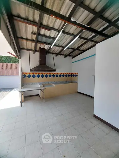 Spacious outdoor kitchen with tiled floor and colorful backsplash under a metal roof.