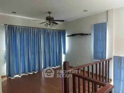 Spacious living room with wooden flooring and blue curtains, featuring a ceiling fan and modern shelving.