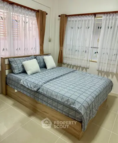 Cozy bedroom with stylish bedding and natural light from two windows.