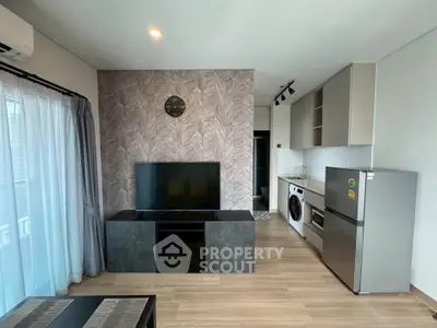 Modern living room with stylish decor, featuring a wall-mounted TV, sleek furniture, and a compact kitchen area.