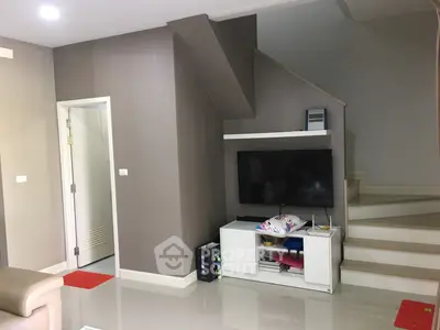 Spacious living room with modern design, glossy tiled flooring, and a custom entertainment unit under a stylish staircase.