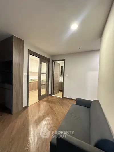 Modern apartment interior with cozy living room and view into a sleek kitchen, featuring wooden flooring and stylish decor.