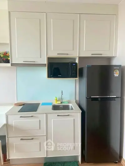 Modern compact kitchen with sleek cabinets, microwave, and fridge in a stylish apartment.