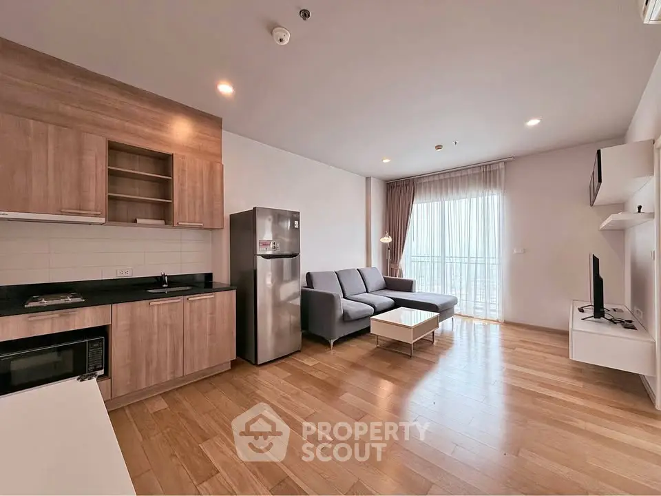 Modern open-plan living room with sleek kitchen and cozy seating area, featuring wooden flooring and natural light.