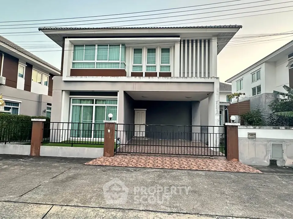 Modern two-story house with gated driveway and large windows in suburban neighborhood.