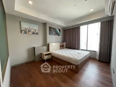 Spacious bedroom with wooden flooring and large window offering city views, perfect for urban living.