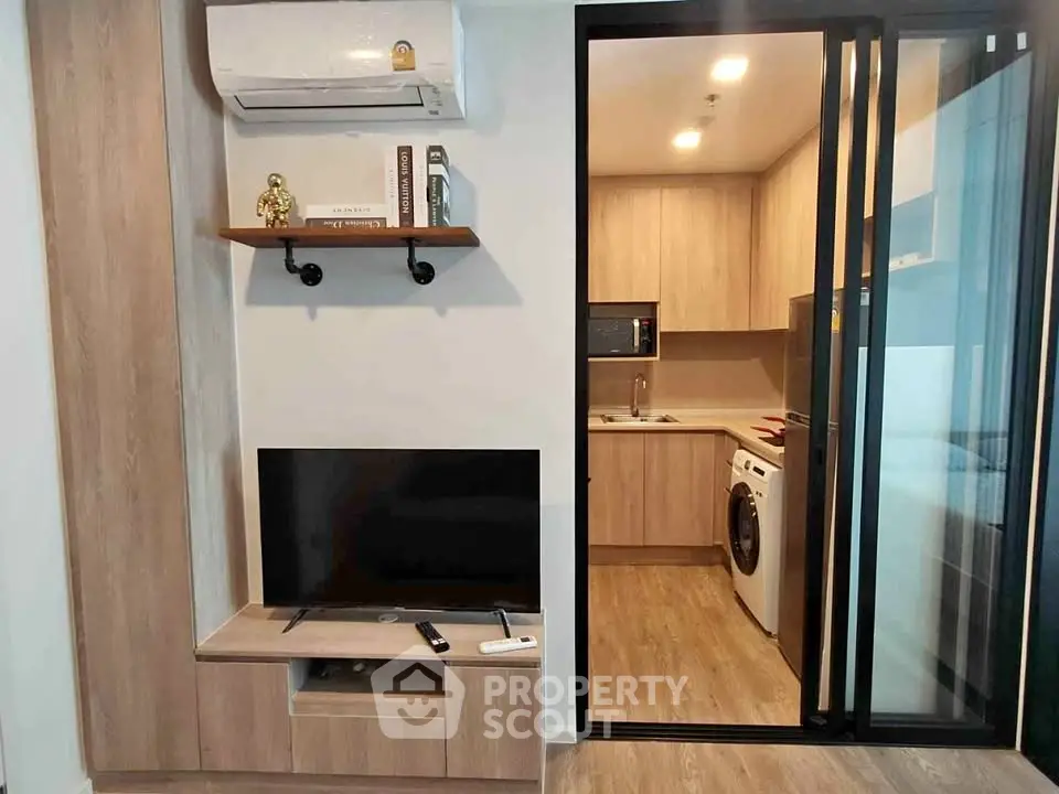 Modern living room with TV and kitchen view, featuring stylish wooden cabinets and appliances.
