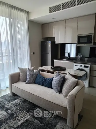 Modern living room with integrated kitchen, featuring sleek appliances and stylish sofa in a bright, airy space.