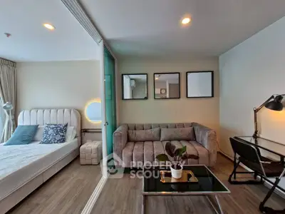 Modern studio apartment with stylish living area and cozy bedroom separated by glass partition.