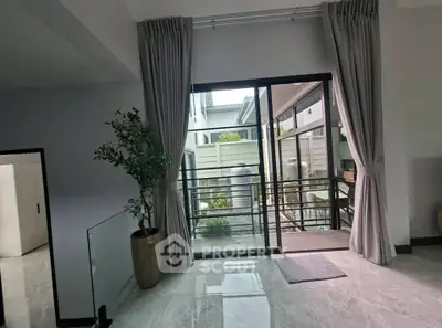 Spacious modern living room with large glass doors opening to a balcony, featuring elegant curtains and a potted plant.