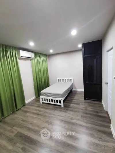 Spacious bedroom with modern flooring and green curtains, featuring a single bed and air conditioning.