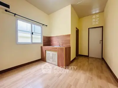 Charming minimalist kitchen with wooden flooring and ample natural light, perfect for cozy living.