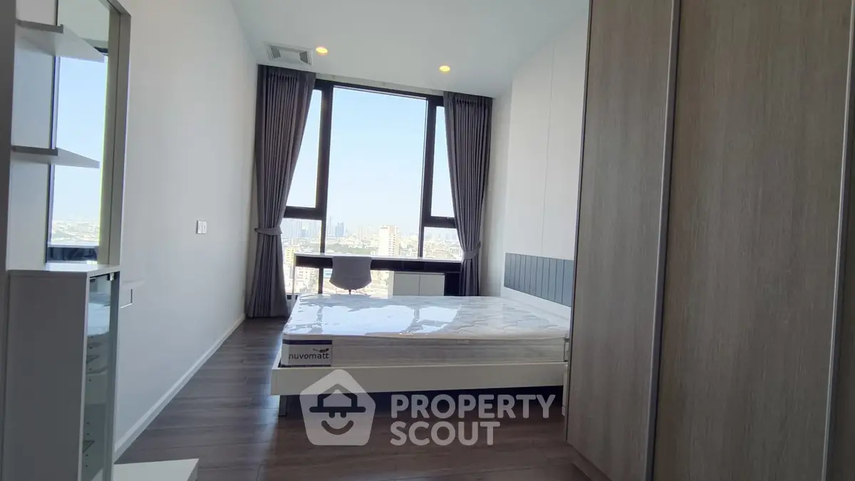 Modern bedroom with large windows and city view, featuring sleek furniture and natural light.
