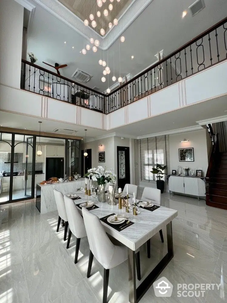 Luxurious double-height dining room with elegant marble flooring, modern chandelier, and grand staircase leading to an ornate balcony overlooking the space.