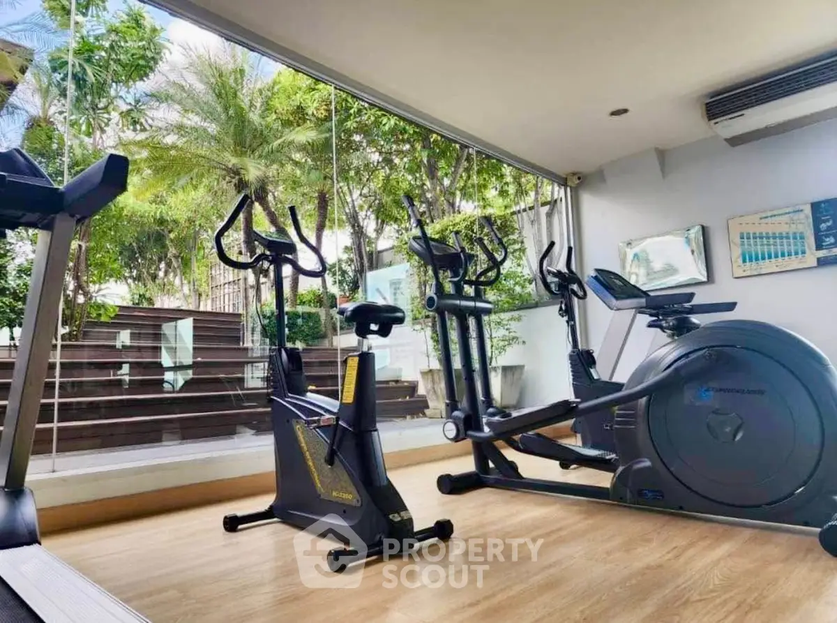 Modern gym with exercise equipment and large windows overlooking greenery