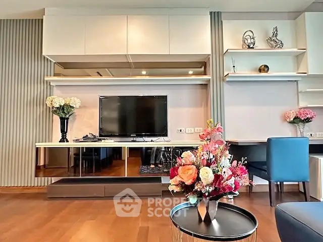 Modern living room with elegant decor and flat-screen TV, featuring stylish shelving and vibrant floral arrangements.