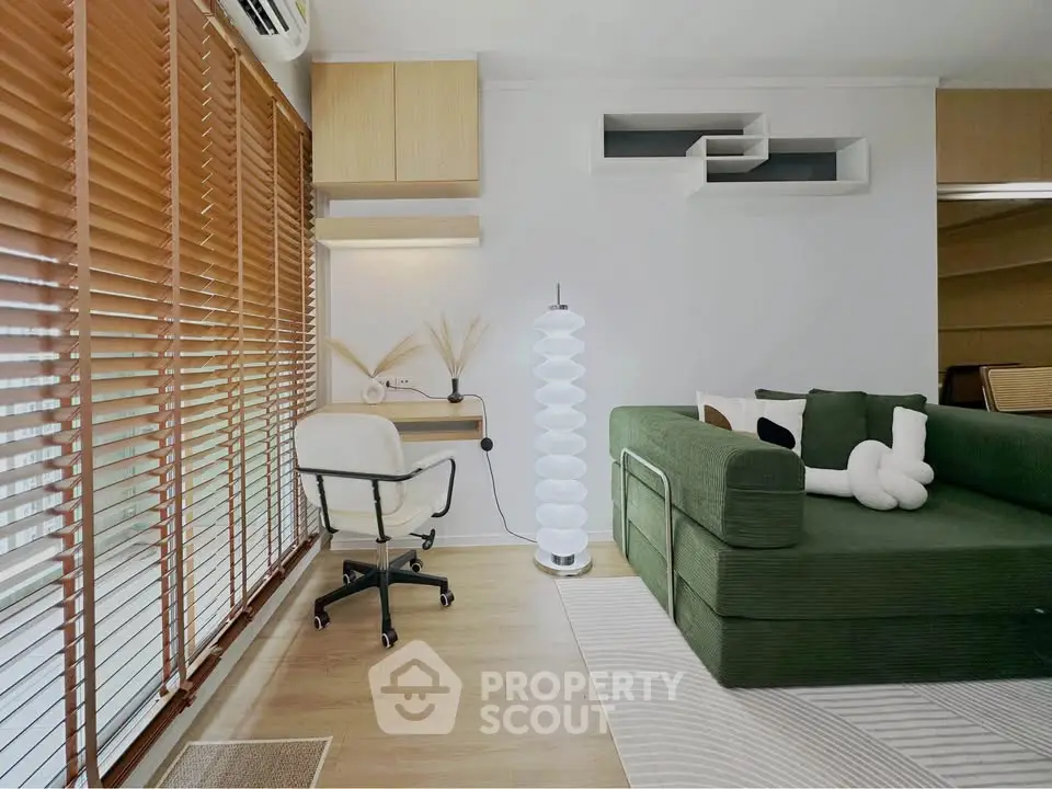 Modern living room with green sofa, stylish decor, and natural light from large windows with blinds.