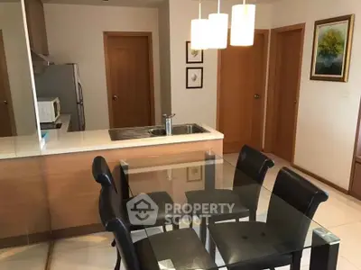 Modern dining area with glass table and leather chairs adjacent to a sleek kitchen.