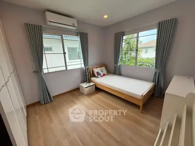 Cozy bedroom with single bed, large windows, and wooden flooring in a bright home.