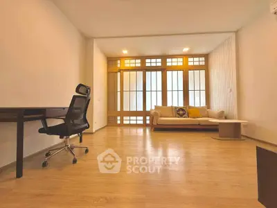 Spacious living room with modern decor and wooden flooring, featuring a comfortable sofa and office chair.