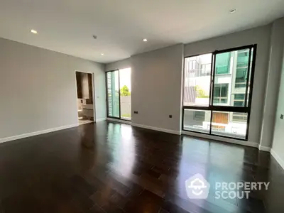 Spacious living room with gleaming hardwood floors, abundant natural light, and a modern, open layout leading to a cozy balcony.