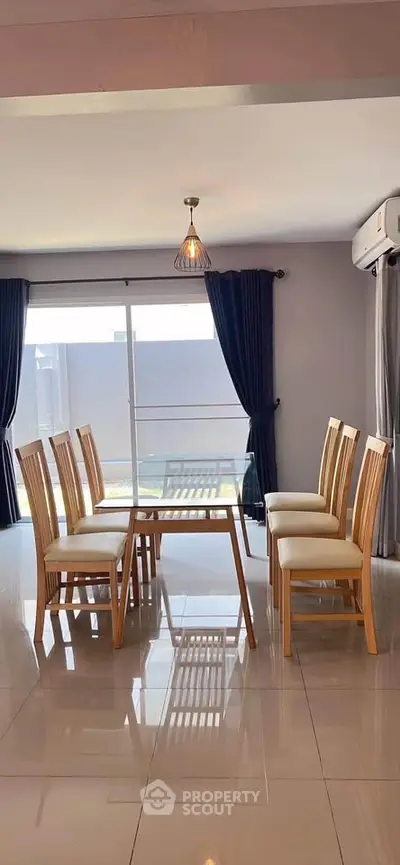 Elegant dining area with glass table and wooden chairs, featuring modern lighting and large windows.