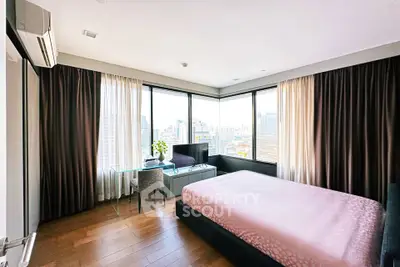 Spacious bedroom with panoramic city views and modern furnishings in a high-rise apartment.
