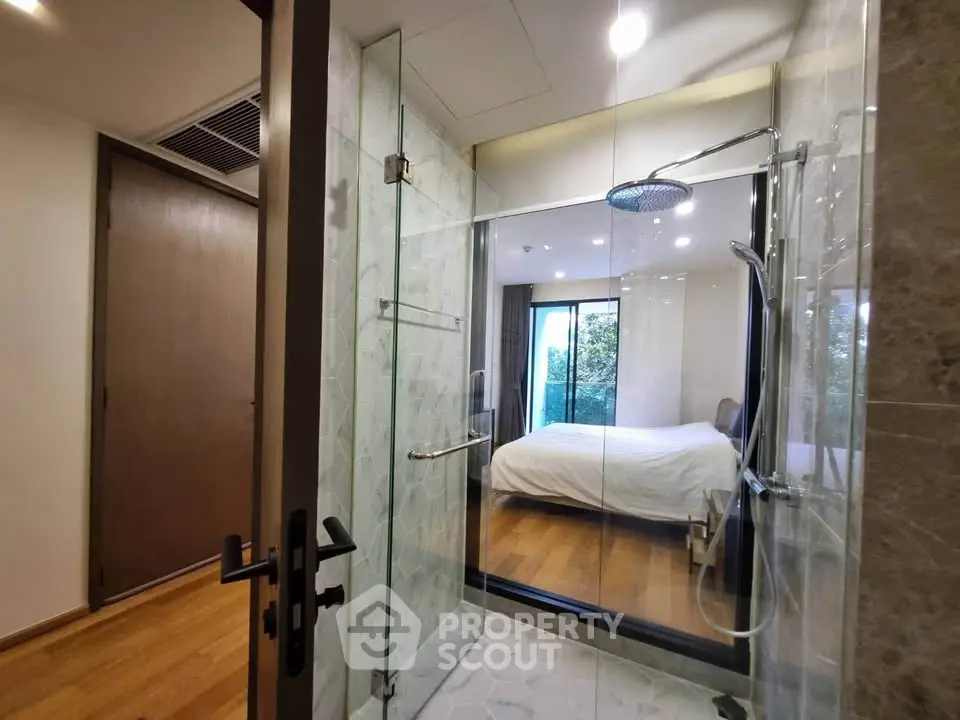 Modern bathroom with glass shower and view into a cozy bedroom with natural light.