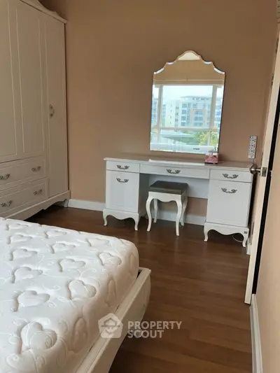 Elegant bedroom with classic white furniture and hardwood flooring, featuring a stylish vanity and large wardrobe.