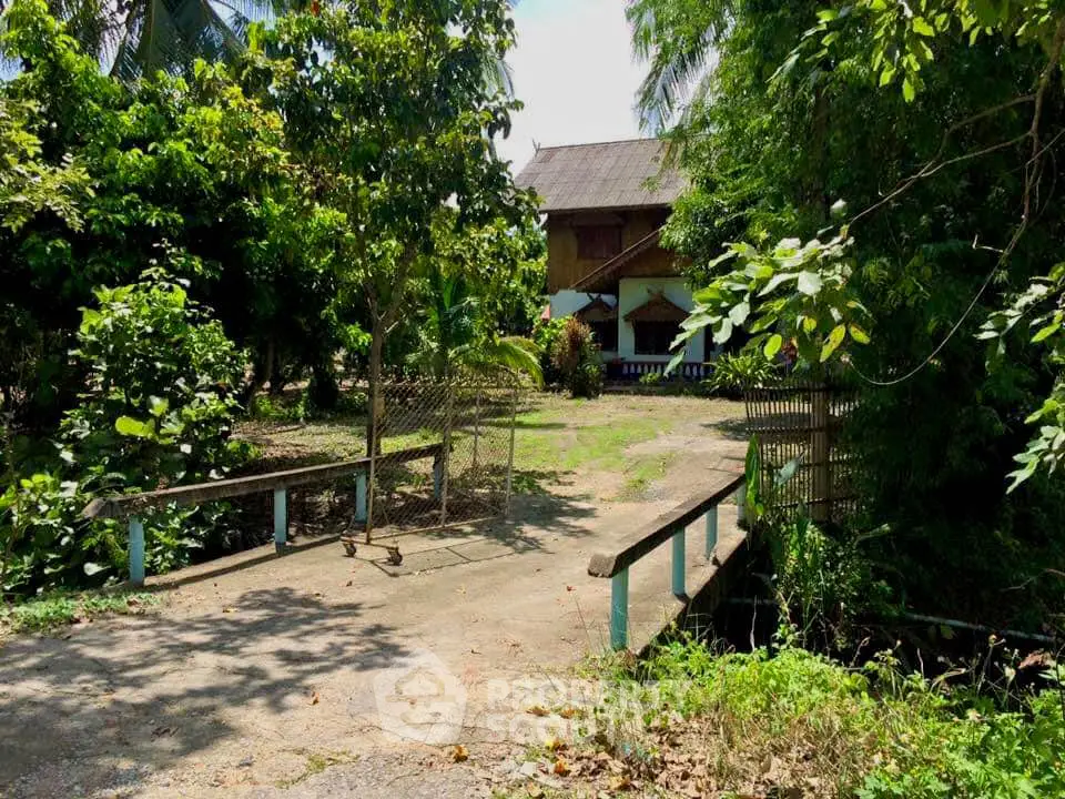 Charming rustic property surrounded by lush greenery and a quaint wooden bridge leading to the entrance.