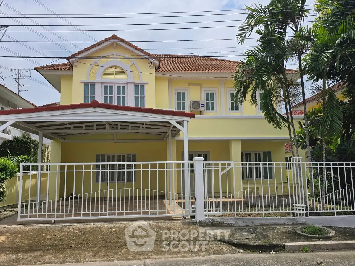 Charming yellow two-story house with gated driveway and lush greenery