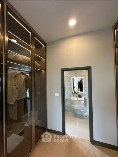 Luxurious walk-in closet with elegant lighting and mirrored entrance to bathroom.