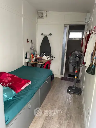 Compact bedroom with single bed, desk, and fan in cozy apartment