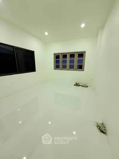 Spacious empty room with glossy white flooring and large windows.