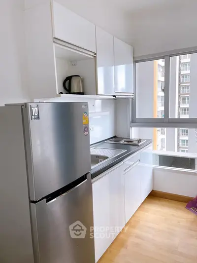 Modern kitchen with sleek white cabinets and stainless steel fridge in a bright apartment.