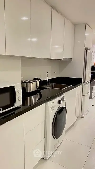 Modern kitchen with sleek white cabinets and built-in appliances, featuring a washing machine and microwave.