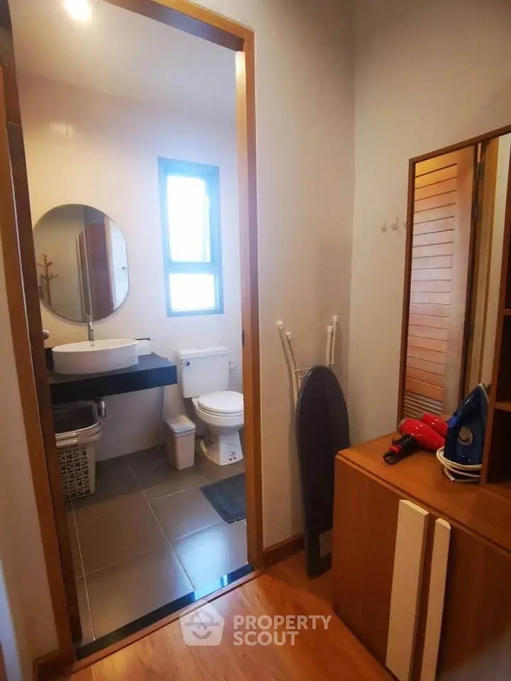 Cozy bathroom with modern fixtures and wooden accents, featuring a round mirror and ample natural light.