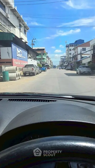 Street view of residential area with parked cars and buildings under blue sky.