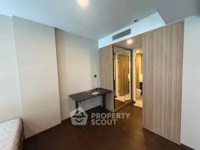 Modern bedroom with wooden flooring and built-in wardrobe, featuring a sleek desk and mirror.