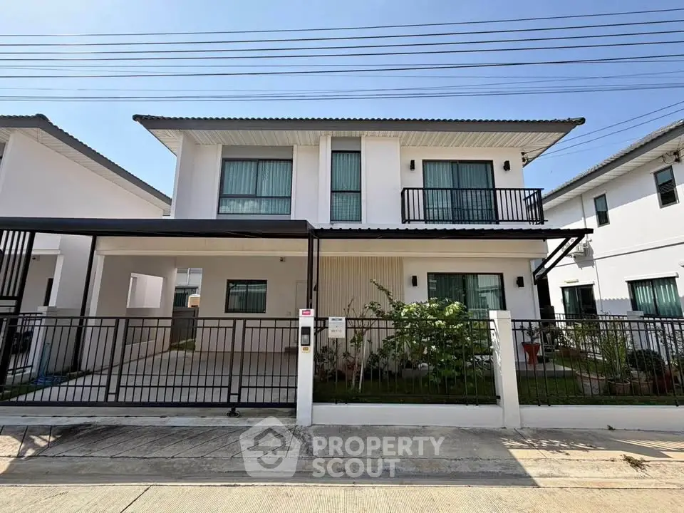 Modern two-story house with balcony and gated driveway in a suburban neighborhood.