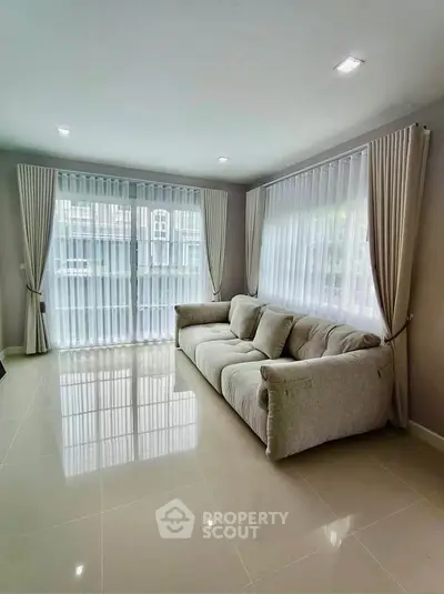 Spacious living room with large windows and elegant curtains, featuring a cozy sofa and glossy tiled floor.