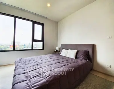 Modern bedroom with large window and stylish decor in urban apartment.