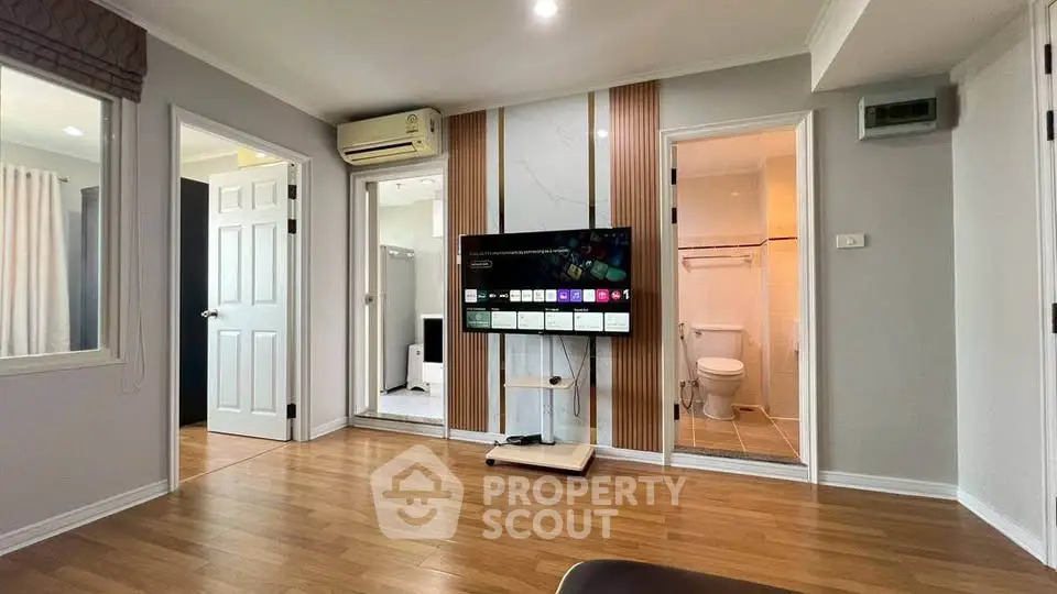 Modern living room with wooden flooring, TV, and access to bathroom and bedroom.